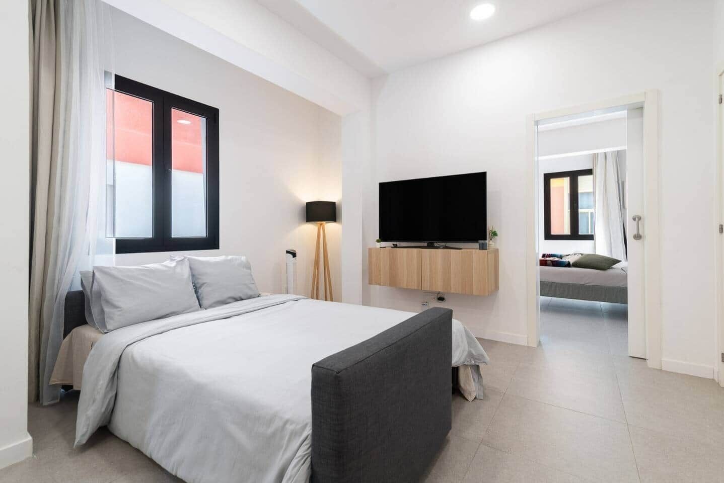 A modern hotel room with a bed, a TV mounted on the wall, and a view of the outside through a window.
