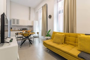 A modern living room with a yellow sofa, a dining area with a table and chairs, and a kitchen in the background. - Apartment 100 m from Las Canteras - Shared Terrace (Las Palmas de Gran Canaria)