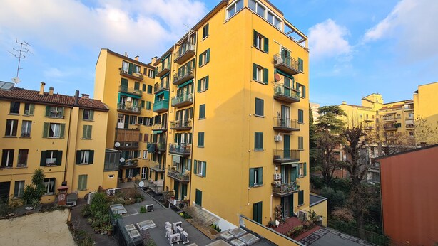 Un edificio amarillo de varios pisos con balcones, un jardín en la azotea y cielo despejado.