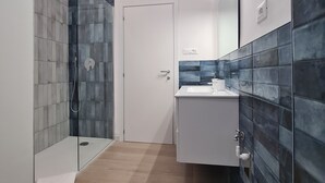 Un baño moderno con ducha envuelta en vidrio, un lavamanos blanco y paredes cubiertas de azulejos azul oscuro.
