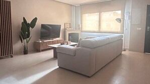 Ein modernes Wohnzimmer mit einem großen weißen Sofa, einem Flachbildfernseher, einem Couchtisch und einer Zimmerpflanze.