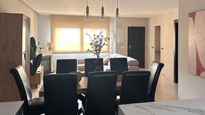Ein stilvoller Essbereich mit einem Marmortisch und schwarzen Stühlen, im Hintergrund eine Küche und ein großes Fenster mit hellem Tageslicht.