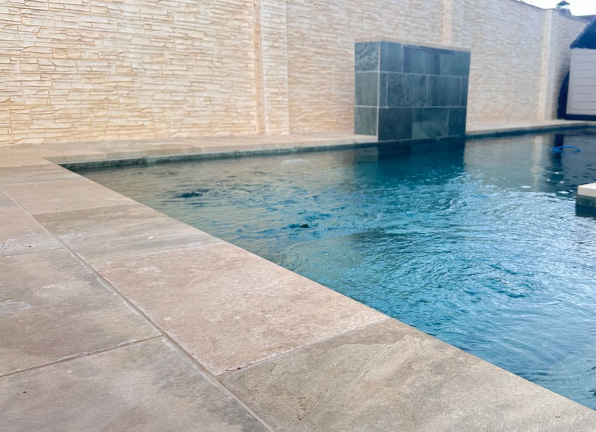 Une piscine avec un mur en pierre et des marches carrelées menant à l’eau.