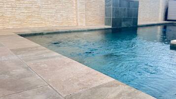 Une piscine avec un mur en pierre et des marches carrelées menant à l’eau.
