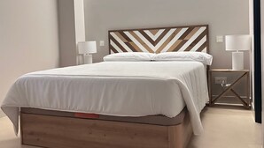 Ein ordentlich bezogenes Bett mit einem Holzkopfteil, zwei Nachttischlampen und einem Nachttisch mit Lampe.