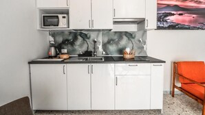 Eine kleine Küche mit weißen Schränken, einer Mikrowelle, einem Spülbecken und einer Marmor-Spritzschutzwand.