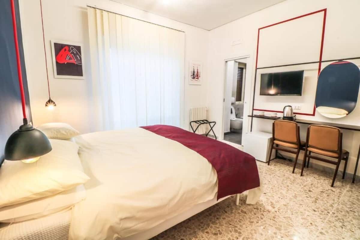 A hotel room with a bed, a desk, a chair, a television, and a mirror.