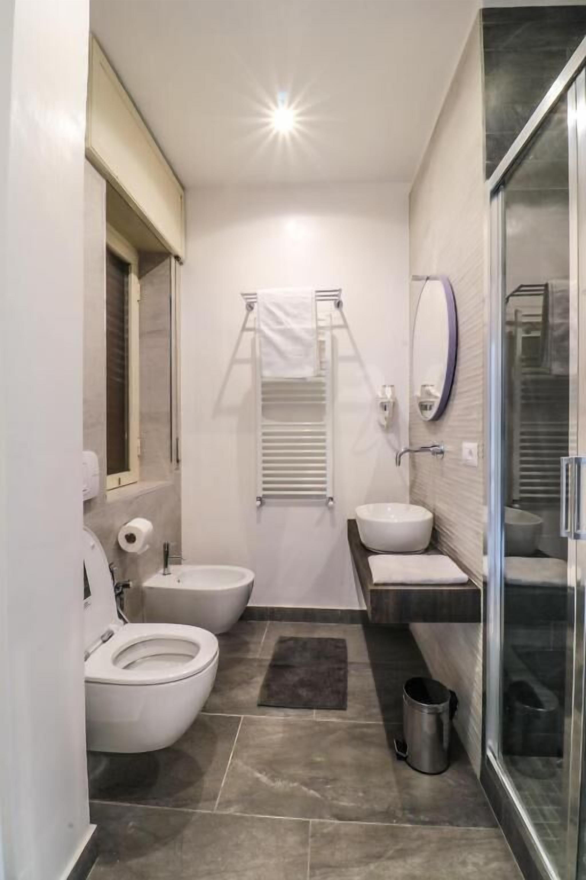 A modern bathroom with a toilet, bidet, sink, and shower area.