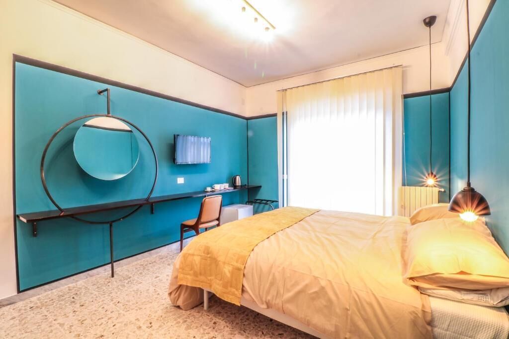 Een slaapkamer met een bed, een bureau, een stoel, een spiegel en een raam met gordijnen.