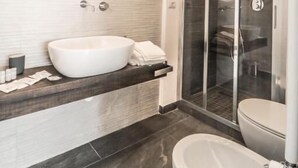 Ein modernes Badezimmer mit einem großen, ovalen Waschbecken, einem runden Spiegel, einer Duschkabine und einer separaten Toilette.