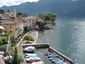 A lakeside town with buildings along the shore, boats docked at the pier, and mountains in the background.
