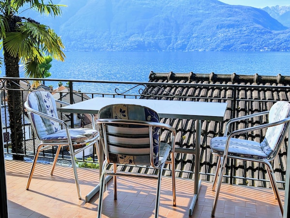 A terrace with a table and chairs, overlooking a body of water and mountains.