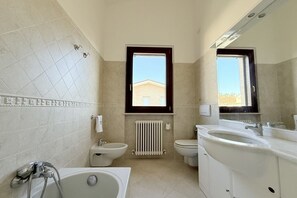 Un bagno con vasca, due servizi igienici, bidet, termosifone e finestra.