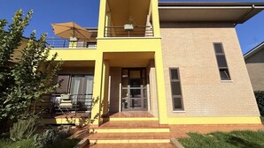 Een gebouw met twee verdiepingen, een gele gevel, een balkon met een parasol en een voordeur.