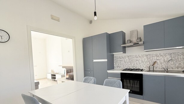 Een moderne keuken met grijze kastjes, een wit aanrechtblad en een marmeren spatwand.