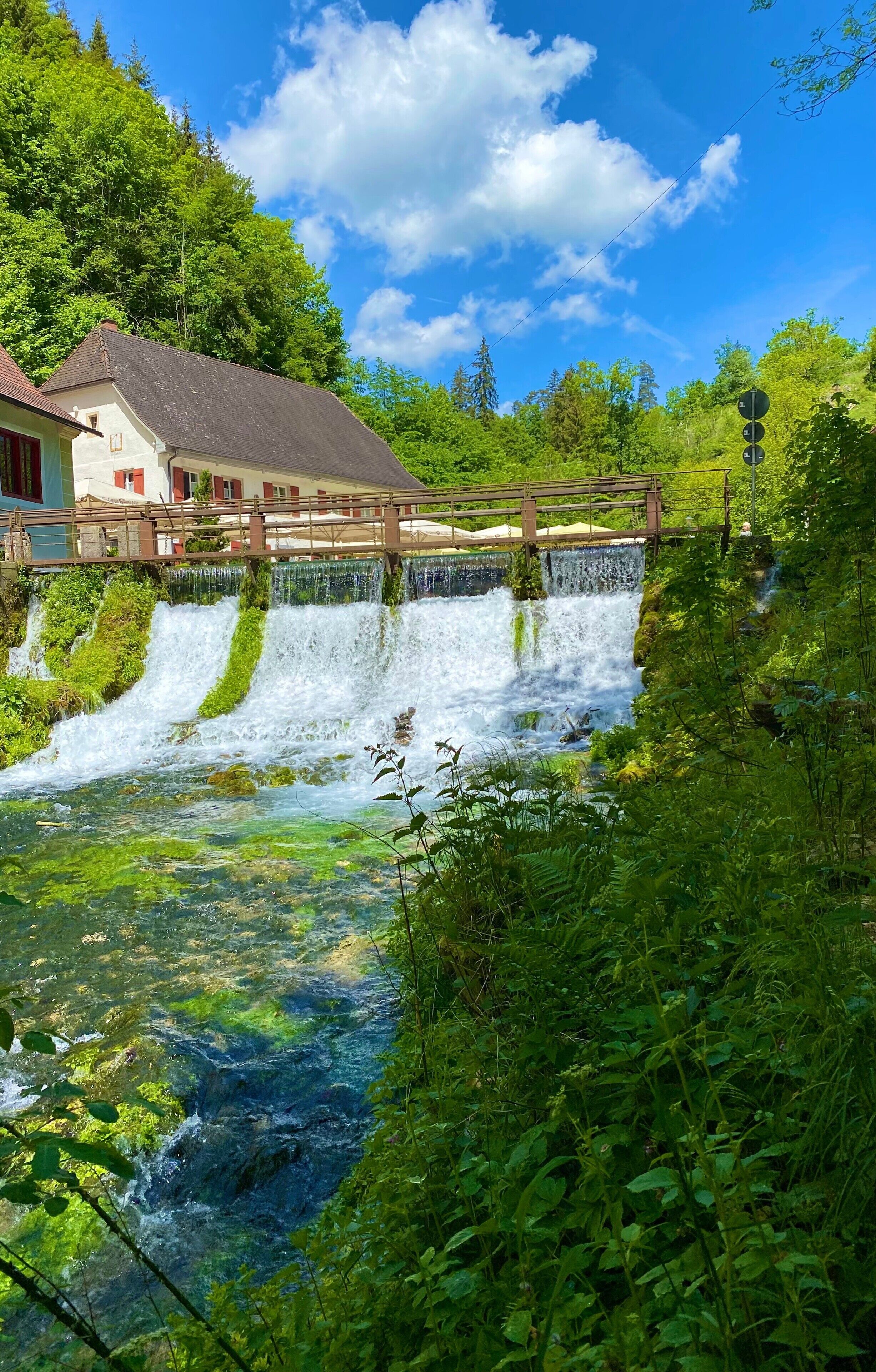 Una cascata, un ponte di legno e un edificio con persiane rosse.