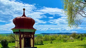 Ein Pavillon mit einer Bank, umgeben von einer Wiese und einem wolkenlosen Himmel.