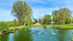 Ein ruhiger Park mit Teich, Bänken und einem kleinen Gebäude.