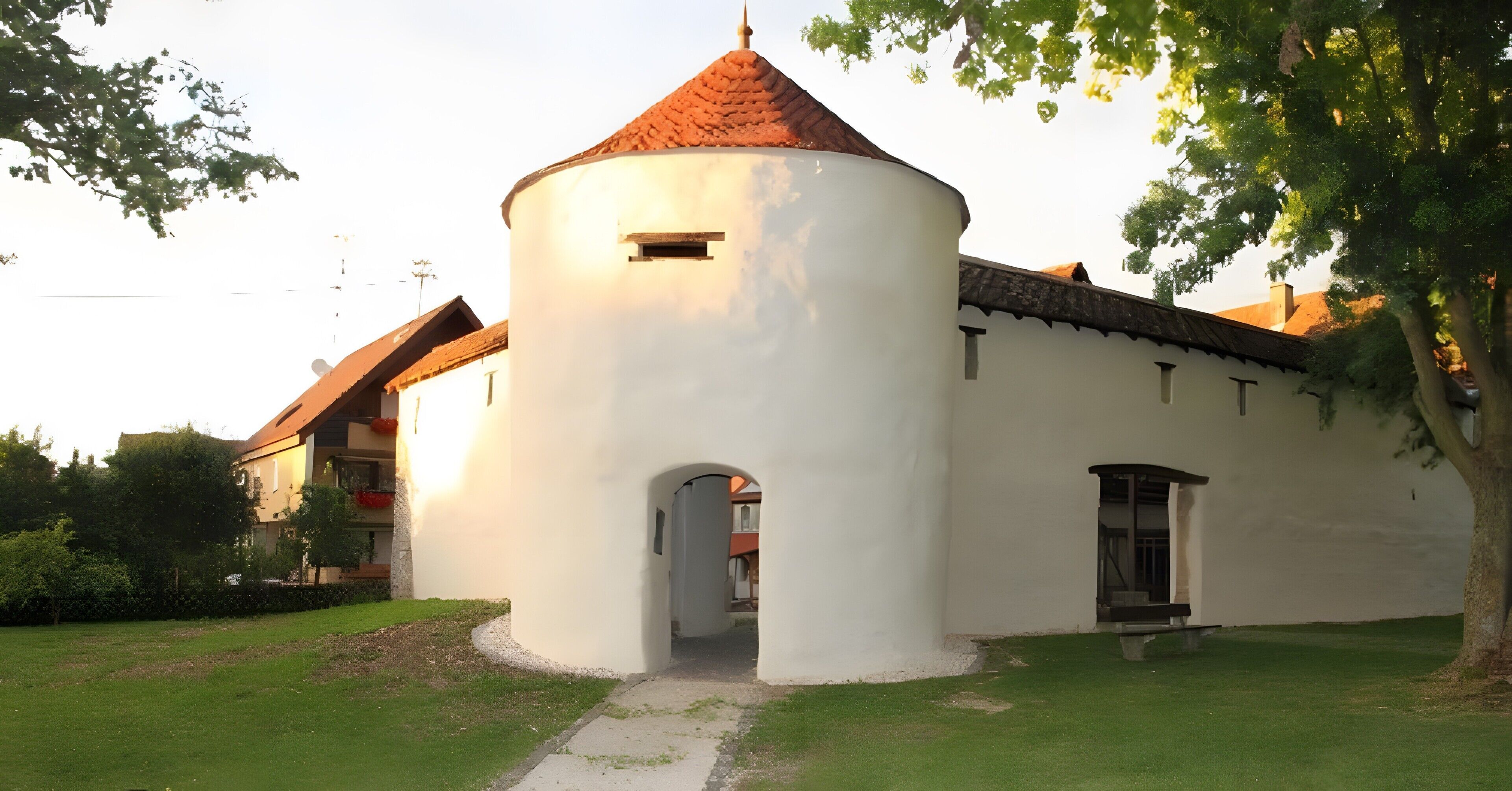 Un bâtiment blanc avec un toit rouge, une tour circulaire et une porte d’entrée.