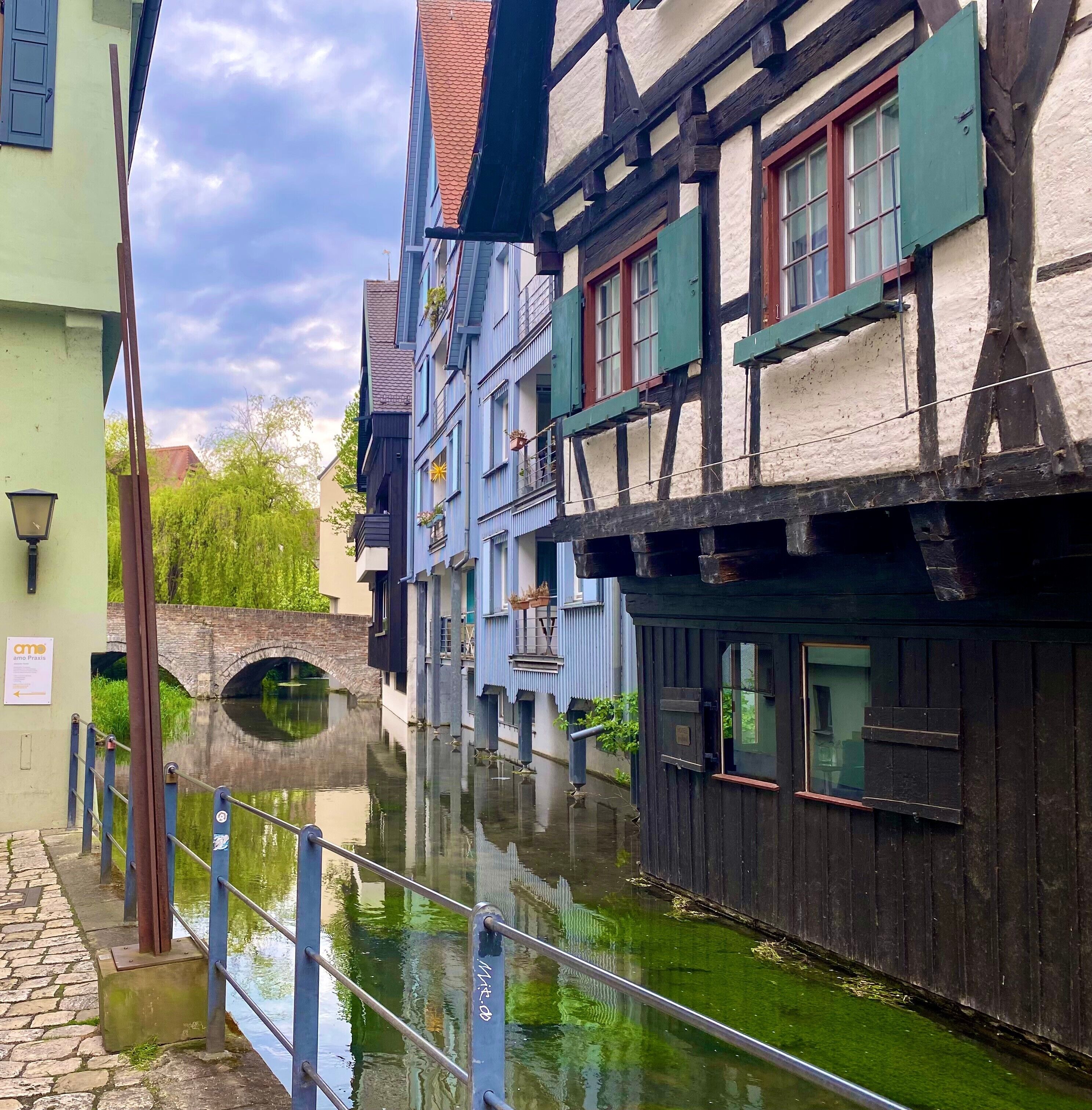 A narrow waterway flanked by traditional half-timbered buildings with a stone bridge in the background.