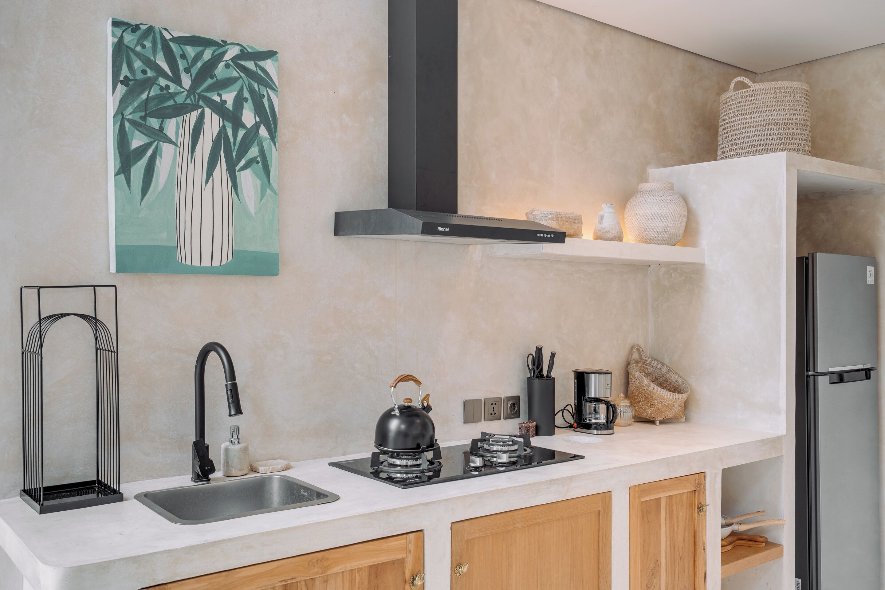 A modern kitchen with a stainless steel sink, a gas stove, wooden cabinets, a black range hood, and a decorative wall piece.