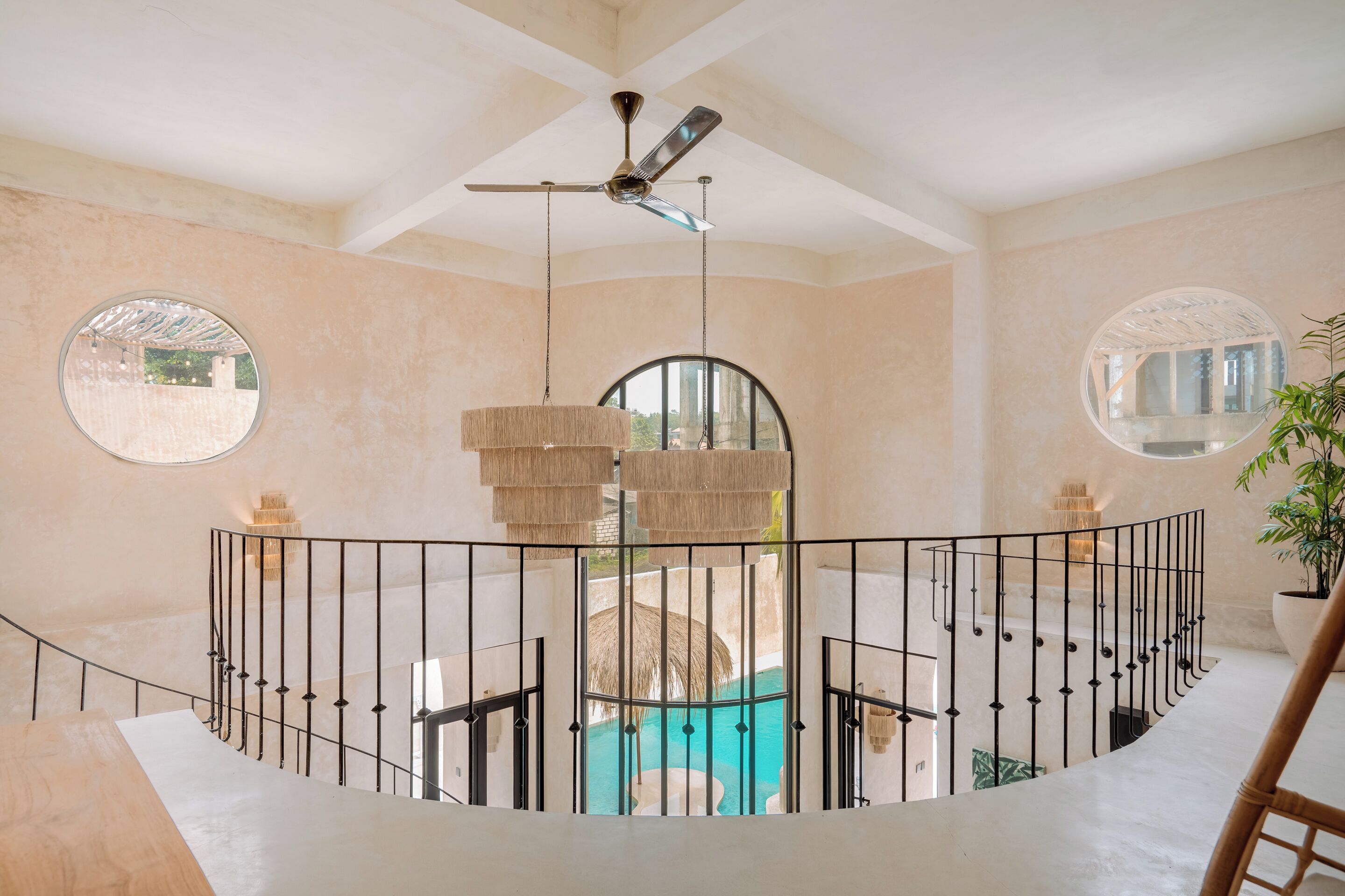 A spacious indoor area with a curved staircase, a ceiling fan, and a view of a swimming pool.