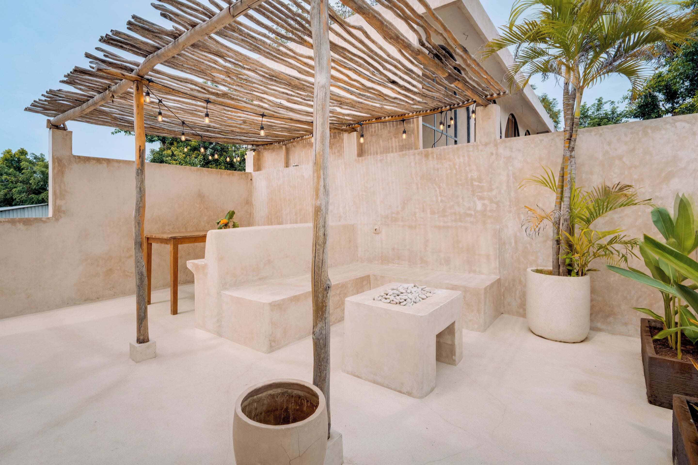 Een overdekt terras buiten, met een pergola, zitplaatsen en potplanten.
