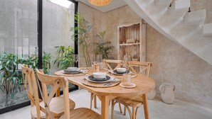 Un espace repas avec une table en bois dressée pour six personnes, entourée de chaises en bois, d’une cloison en verre et offrant une vue sur la verdure à l’extérieur.