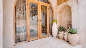 Une entrée d’immeuble avec une porte en bois, de grands pots de plantes et un petit escalier.