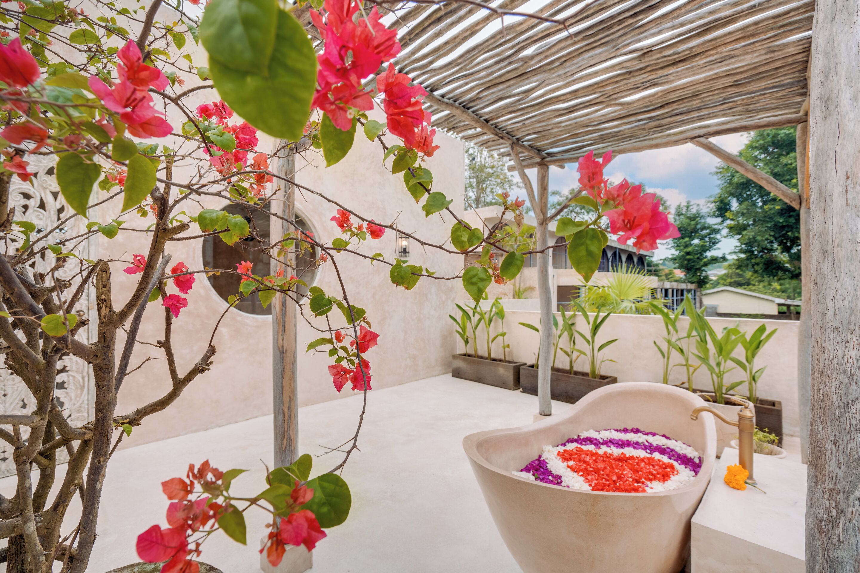 Ein überdachter Außenbereich mit einem großen Pflanzgefäß, gefüllt mit bunten Blumen, einer Wasserspiele und einer Pergola.