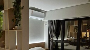 Une chambre d’hôtel moderne dotée d’un grand lit, d’une bibliothèque intégrée, d’une grande fenêtre avec des rideaux et d’un appareil de climatisation fixé au plafond.