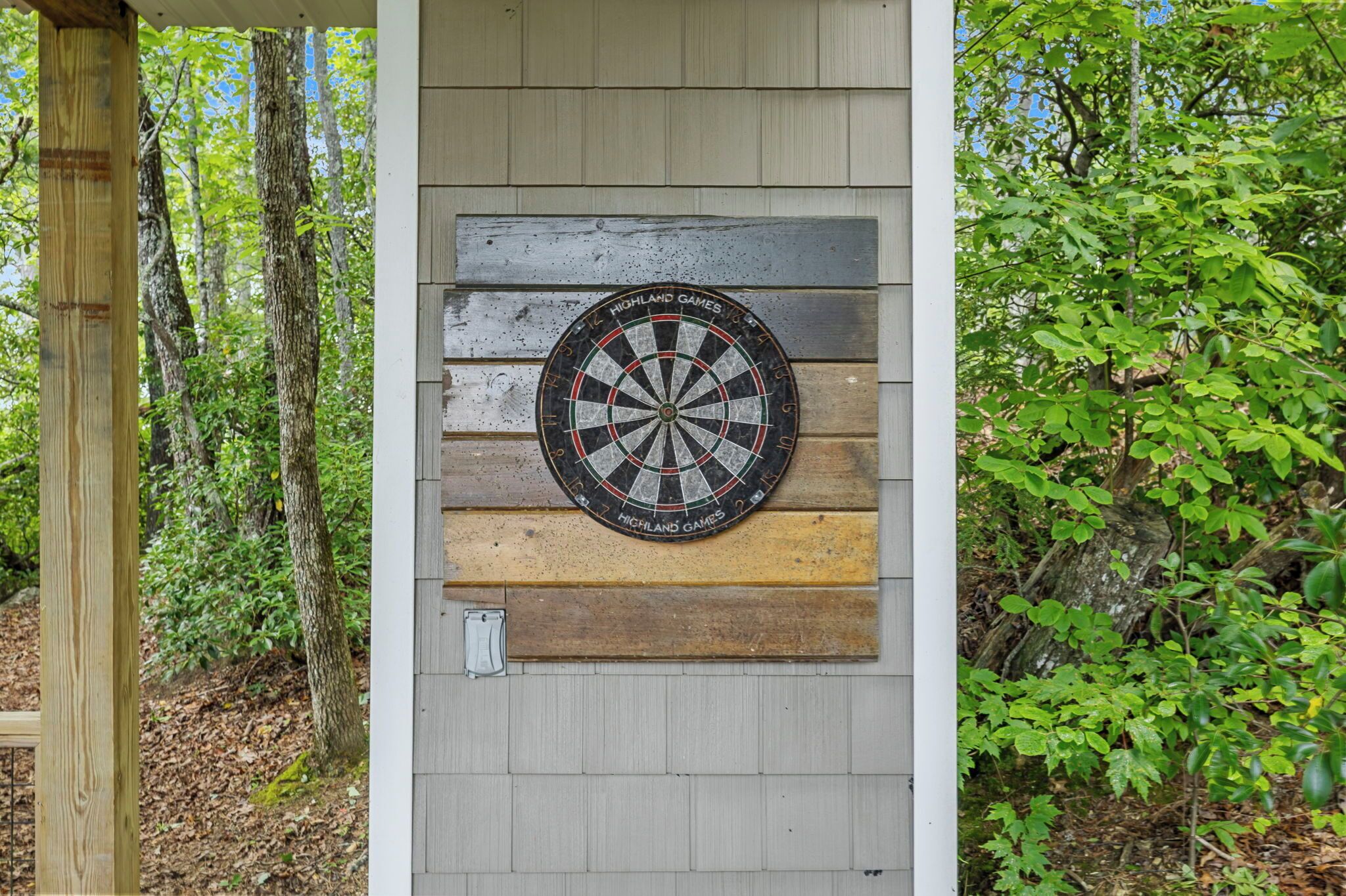 A dartboard mounted on a wooden wall with a natural backdrop of trees and foliage.