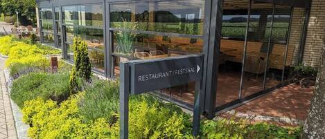 Ein modernes Restaurant mit Glasfassade, umgeben von gepflegten Gärten.