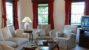 Ein Wohnzimmer mit einer Couch, Sesseln, einem Couchtisch, einer Lampe und einem Fernseher.
