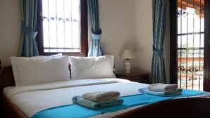 Ein Schlafzimmer mit einem Bett, zwei Kissen, einem Nachttisch mit Lampe und Vorhängen.