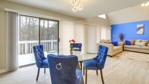 A modern living room with a glass dining table, blue upholstered chairs, a beige sofa, and a large window with blinds. - 4 Mi to Charming Dtwn Fayetteville! Bright Home (Fayetteville)