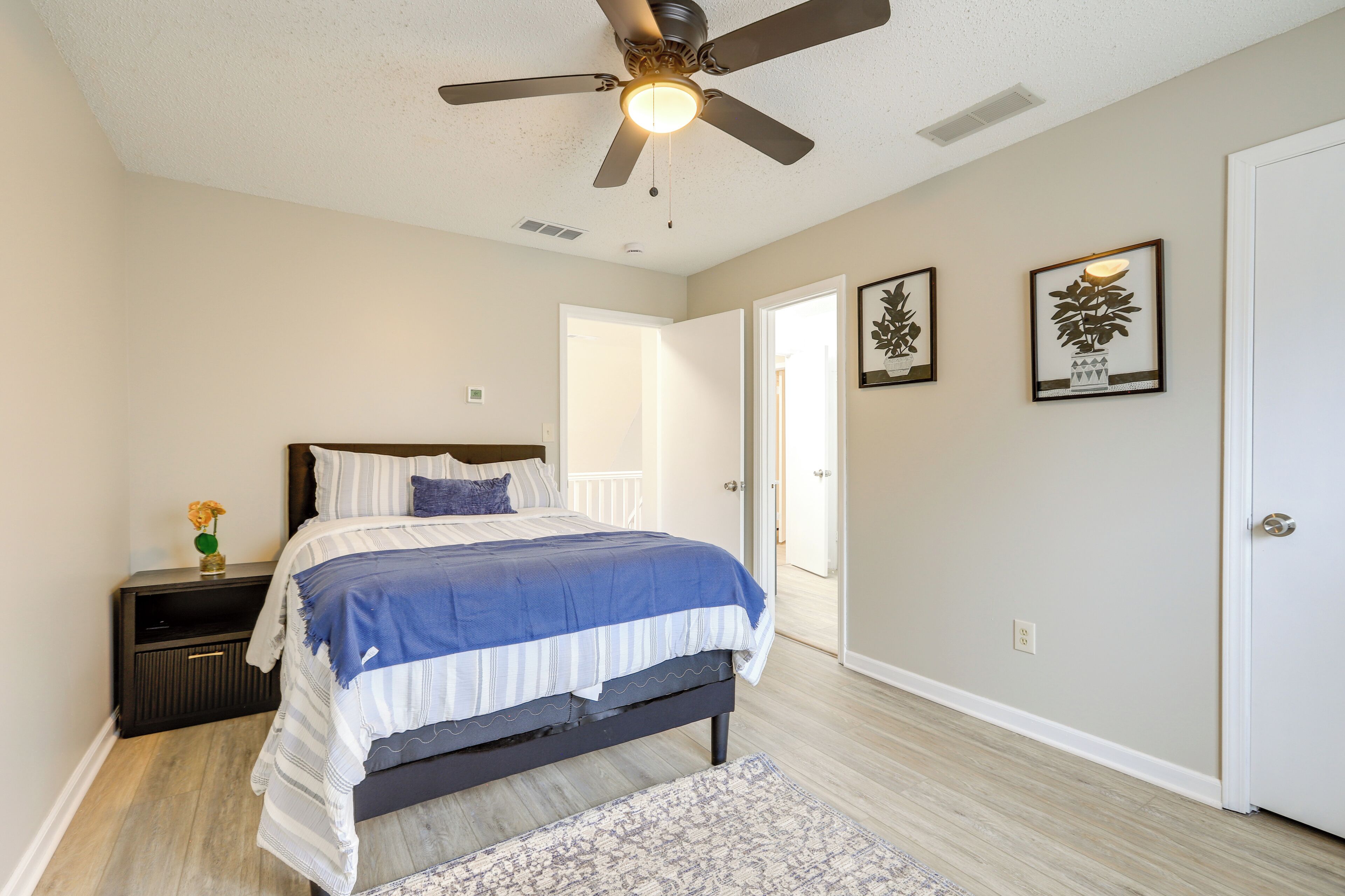 A bedroom with a bed, a nightstand, a ceiling fan, and two framed pictures on the wall.