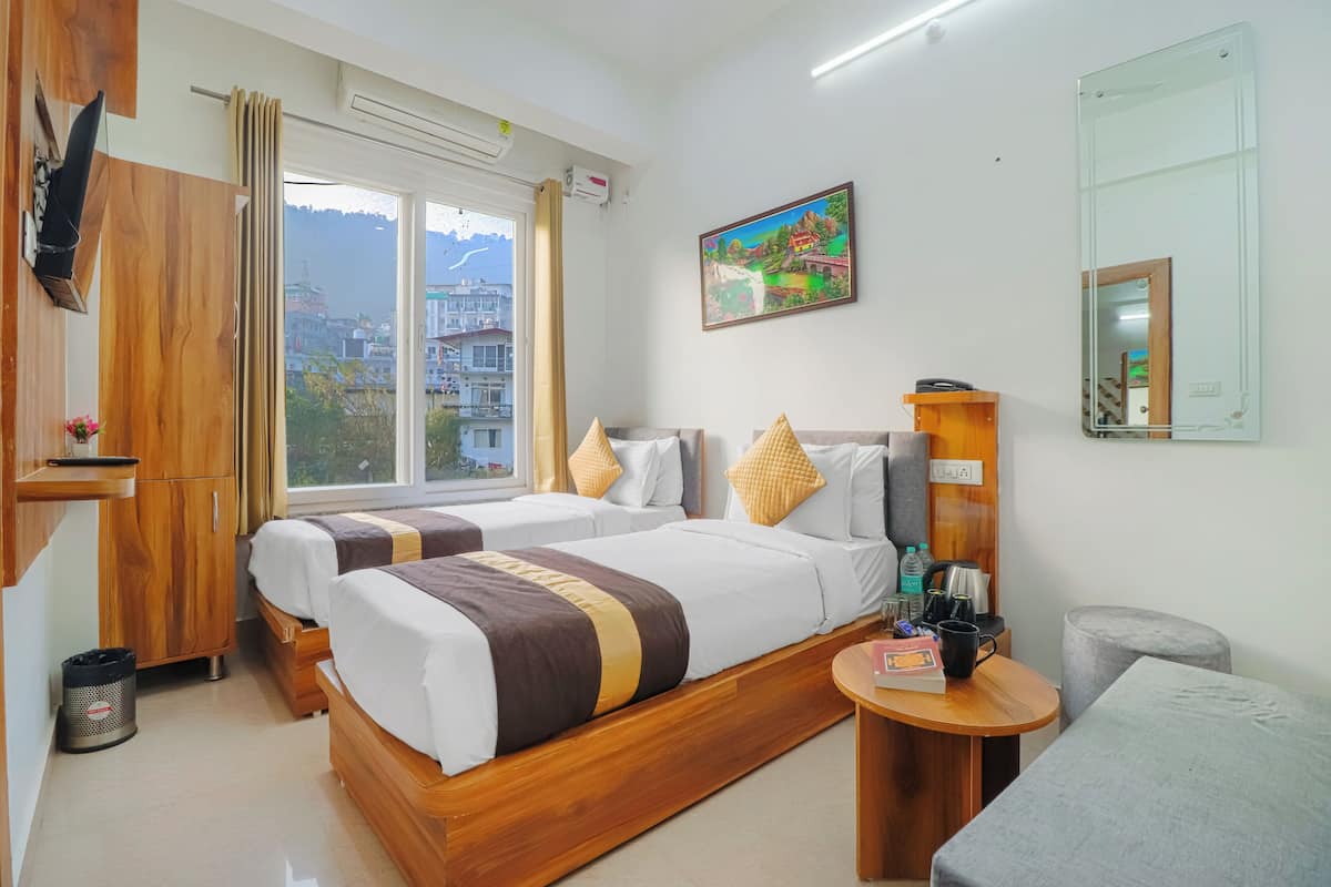 Quarto de hotel com duas camas, um guarda-roupa de madeira, uma mesinha com uma cadeira, um espelho e um quadro na parede.