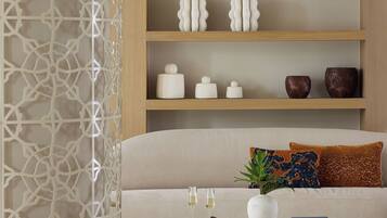 Una sala de estar con un sofá color beige, una mesa de centro blanca y jarrones decorativos en estanterías.