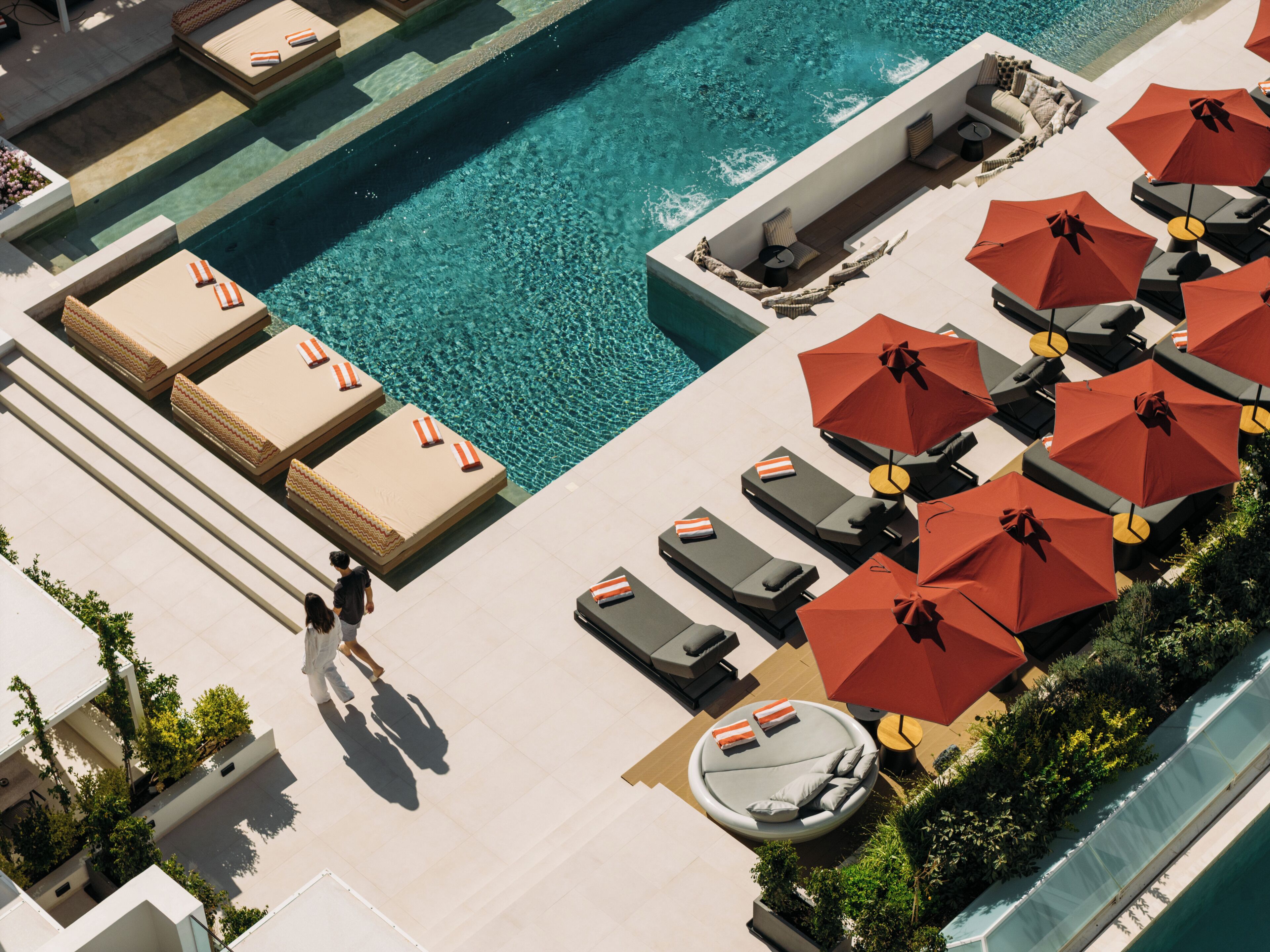 Ein Poolbereich auf dem Dach mit Liegestühlen und Sonnenschirmen, eine Sitzecke mit Sofas und einem Tisch sowie freie Sicht auf den Pool.