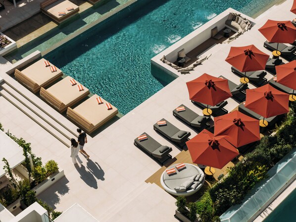 A rooftop pool area with sun loungers and umbrellas, a seating area with sofas and a table, and a clear view of the pool. - Santorini Heart Hotel & Spa (Santorini)