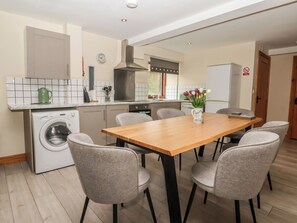 A modern kitchen with a built-in washing machine, a dining table with chairs, and a view of the living area. - Mulberry Manor (Hull)