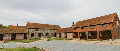 A courtyard with stone buildings, a gravel path, and a grassy area.