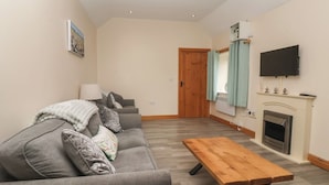 A living room with a sofa, a wooden table, a fireplace, and a TV mounted on the wall. - Meadow View (Hull)