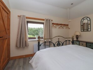 A bedroom with a bed, a window with curtains, a radiator, a mirror, and a wooden wardrobe. - Meadow View (Hull)