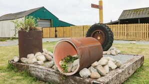 A rustic outdoor setting with a welcome sign, a large tire, and two rusted barrels with plants. - Meadow View (Hull)