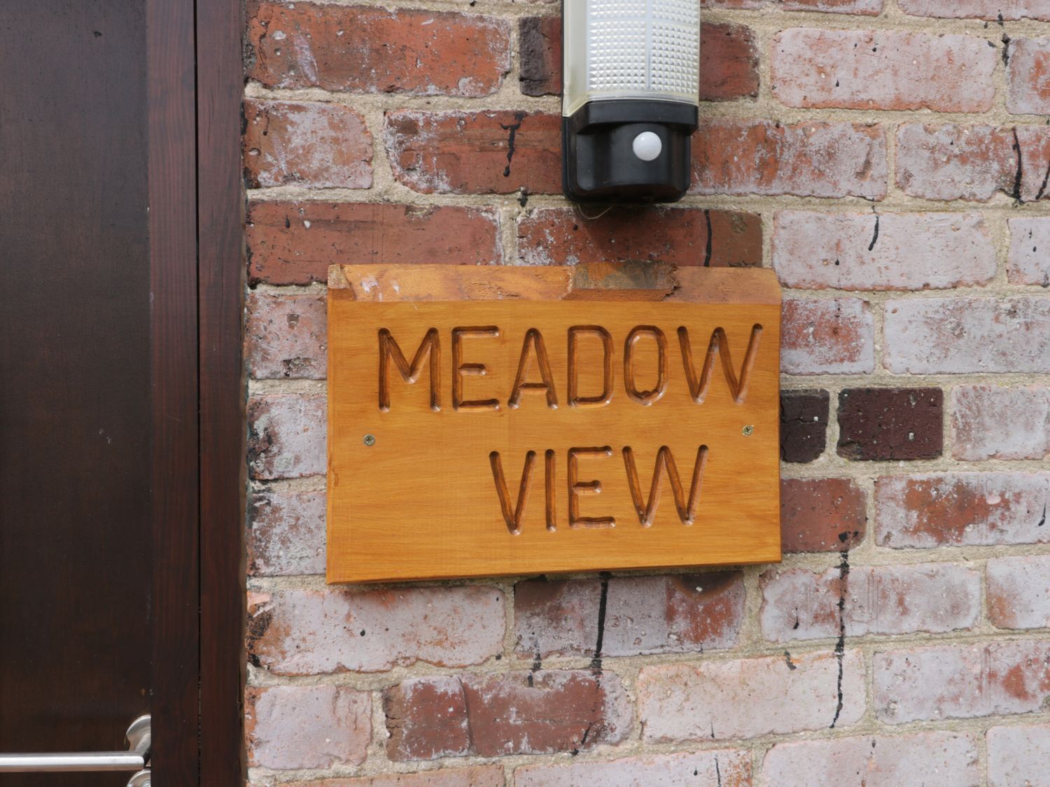 A wooden sign with the text "MEADOW VIEW" mounted on a brick wall.