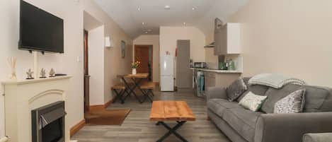 A modern living room with a fireplace, a wooden coffee table, a grey sofa, and a kitchen in the background.