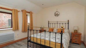 Une chambre à coucher avec un lit, une fenêtre avec des rideaux, un radiateur, une horloge murale et une table de chevet avec une lampe.