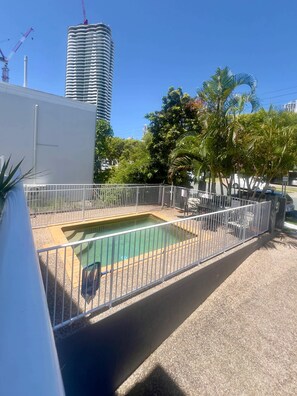 Ein Pool auf dem Dach mit einem Metallzaun, umgeben von Bäumen und einem hohen Gebäude im Hintergrund.